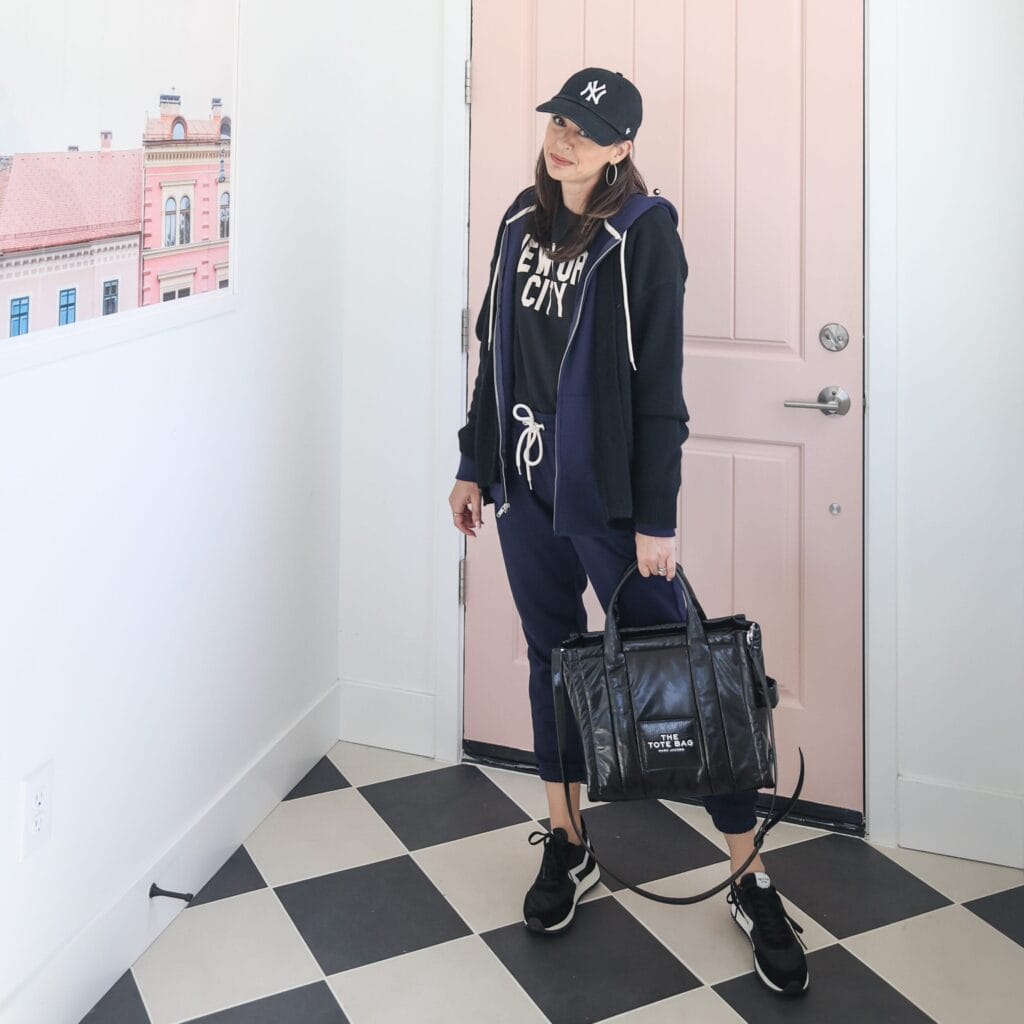 Jen wearing rag and bone retro runner sneakers at pink door holding the tote bag and wearing a yankees baseball hat
