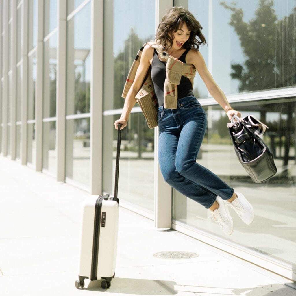 Traveler at the Sacramento International Airport wearing Sam Edelman Sneakers | Paige Jeans | Simms Bodysuit | Burberry Cardigan | Suitcase