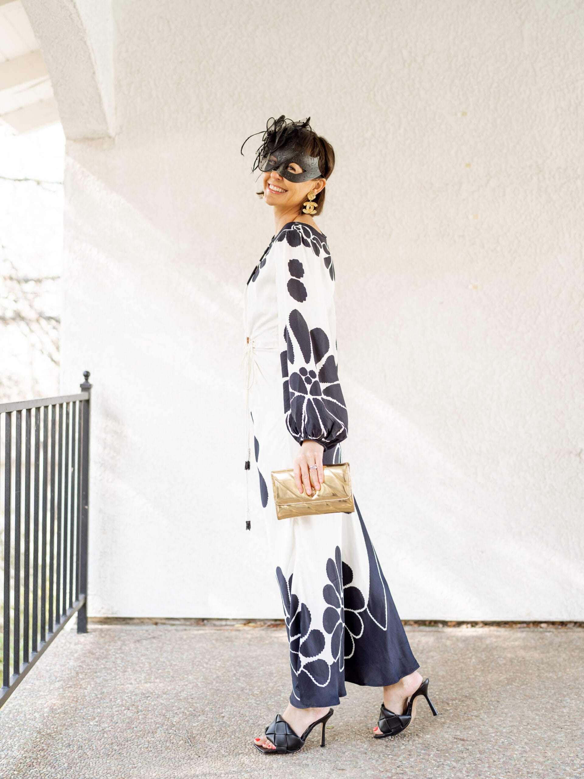 woman at an event wearing a black tie mask and black bottega sandals with gold woc and long black and white maxi dress